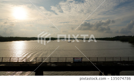 Scenic River Landscape with Old Bridge and Distant Floating Houses at Sunset Scenic River Landscape with Old Bridge and Distant Floating Houses at Sunset 135074786