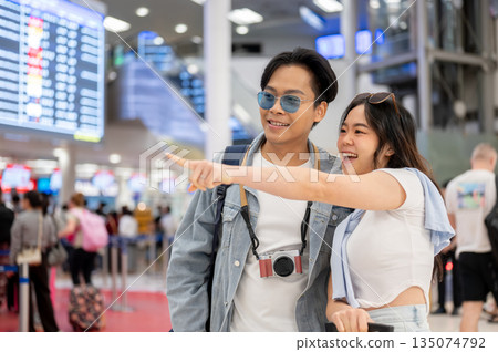 Asian couple tourist woman pointing aside man while going on a trip waiting for departure in airport 135074792