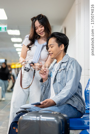Asian tourist couple go on trip a woman showing camera photo to man waiting for departure in airport Asian tourist couple go on trip a woman showing camera photo to man waiting for departure in airport 135074816