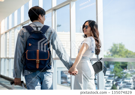 Back view of asian man and woman tourist couple go on a trip holding hands while walking in airport. 135074829