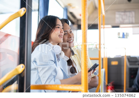Asian tourist couple go on trip woman holding phone man looking ahead while sitting in shuttle bus. 135074862