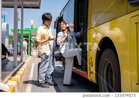 Asian tourist couple man and woman talking before going in or getting on shuttle bus at stop station 135074873