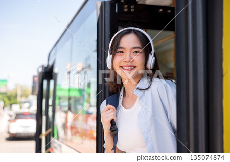Asian woman tourist holding bag strap while going out or getting off the shuttle bus at stop station 135074874