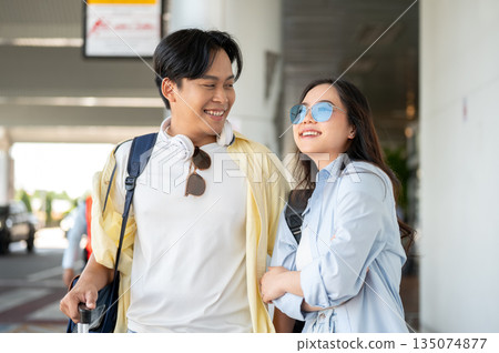 Asian tourist couple go on trip woman crossed arm talking to man dragging luggage walking in airport Asian tourist couple go on trip woman crossed arm talking to man dragging luggage walking in airport 135074877