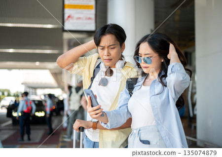 Asian tourist couple man and woman looking at phone in troubled standing waiting for taxi in airport Asian tourist couple man and woman looking at phone in troubled standing waiting for taxi in airport 135074879