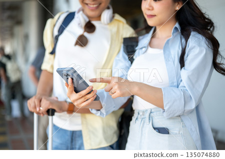 Close up asian tourist couple man woman looking at phone while standing waiting for taxi in airport. 135074880