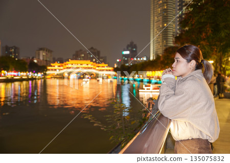 Happy woman traveler travel in Chengdu city. Tourist sightseeing Beautiful Anshun Bridge at night. Famous Landmark for tourism attraction in Sichuan, China Happy woman traveler travel in Chengdu city. Tourist sightseeing Beautiful Anshun Bridge at night. Famous Landmark for tourism attraction in Sichuan, China 135075832