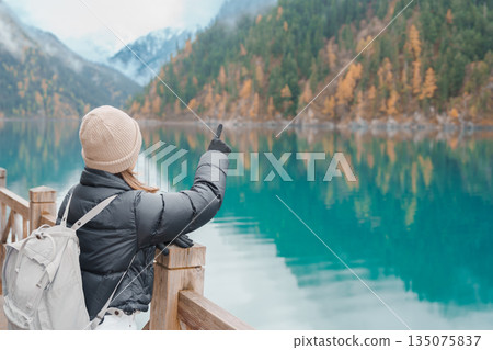 Happy woman traveler travel in jiuzhaigou national park in Sichuan, China. Tourist sightseeing Long lake and snow mountain in Autumn season. Famous Landmark and Vacation near Chengdu, China Happy woman traveler travel in jiuzhaigou national park in Sichuan, China. Tourist sightseeing Long lake and snow mountain in Autumn season. Famous Landmark and Vacation near Chengdu, China 135075837