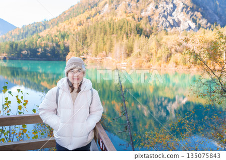 Happy woman traveler travel in jiuzhaigou national park in Sichuan, China. Tourist sightseeing Arrow Bamboo lake and snow mountain in Autumn season. Famous Landmark and Vacation near Chengdu, China Happy woman traveler travel in jiuzhaigou national park in Sichuan, China. Tourist sightseeing Arrow Bamboo lake and snow mountain in Autumn season. Famous Landmark and Vacation near Chengdu, China 135075843