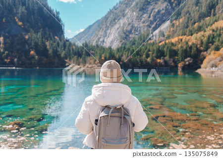 Happy woman traveler travel in jiuzhaigou national park in Sichuan, China. Tourist sightseeing Five Flower lake and snow mountain in Autumn season. Famous Landmark and Vacation near Chengdu, China 135075849