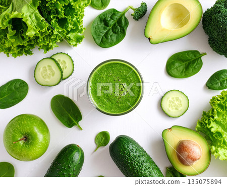 Direct overhead view of a healthy green smoothie in a glass surrounded by fresh vegetables on a white table, sunlight 135075894