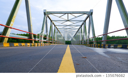 Low Angle Perspective of Steel Truss Bridge and Asphalt Road with Yellow Line 135076082
