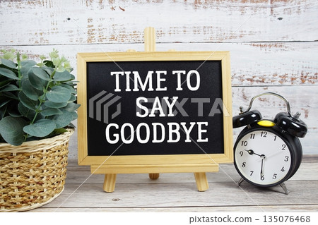 Time to say Goodbye text written on blackboard with alarm clock on wooden background 135076468