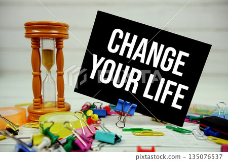 Change Your Life text on paper card with hourglass and stationary on wooden background Change Your Life text on paper card with hourglass and stationary on wooden background 135076537