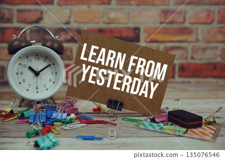Learn from Yesterday text on paper card with alarm clock and stationary on wooden background 135076546