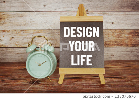 Design Your Life text on easel blackboard with alarm clock on wooden background Design Your Life text on easel blackboard with alarm clock on wooden background 135076676