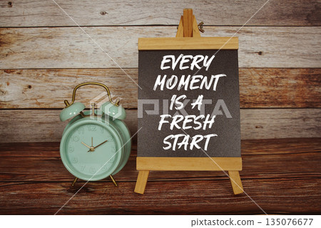 Every Moment Is A Fresh Start text on easel blackboard with alarm clock on wooden background Every Moment Is A Fresh Start text on easel blackboard with alarm clock on wooden background 135076677