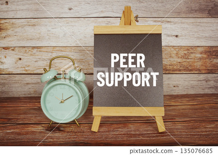 Peer Support text on easel blackboard with alarm clock on wooden background Peer Support text on easel blackboard with alarm clock on wooden background 135076685