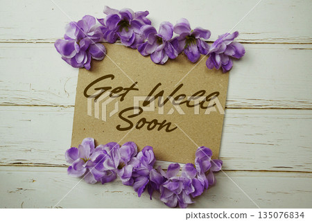 Get Well Soon text written on paper card with flower decoration on wooden background 135076834