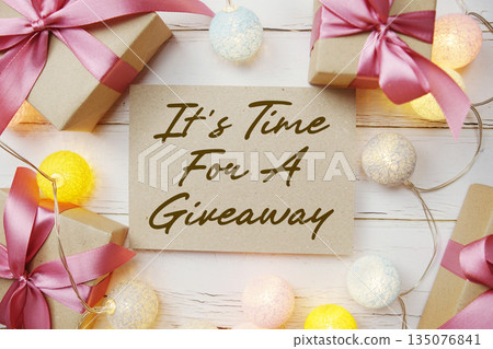 It's Time For A Giveaway text with gift present and LED cotton balls decorate on wooden background It's Time For A Giveaway text with gift present and LED cotton balls decorate on wooden background 135076841