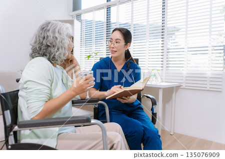 Smiling physiotherapist taking care of the happy senior patient in wheelchair at home. Smiling physiotherapist taking care of the happy senior patient in wheelchair at home. 135076909