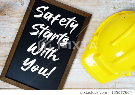 Safety Starts With You! text written on blackboard with safety helmet on wooden background 135077664