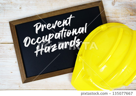 Prevent Occupational Hazards text written on blackboard with safety helmet on wooden background 135077667