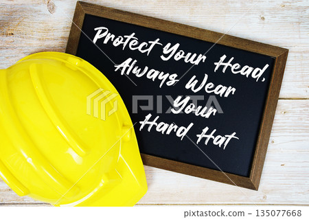 Protect Your Head, Always Wear Your Hard Hat text written on blackboard with safety helmet on wooden background 135077668