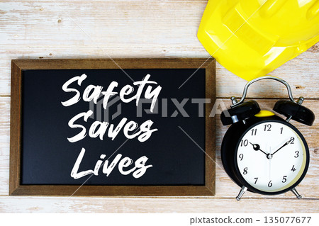 Safety Saves Lives text written on blackboard with safety helmet and alarm clock on wooden background Safety Saves Lives text written on blackboard with safety helmet and alarm clock on wooden background 135077677