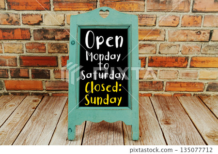 Open Monday to Saturday Closed Sunday text written on wooden board standing with old brick wall background Open Monday to Saturday Closed Sunday text written on wooden board standing with old brick wall background 135077712