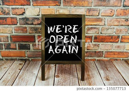 We're Open Again text written on wooden board standing with old brick wall background 135077713