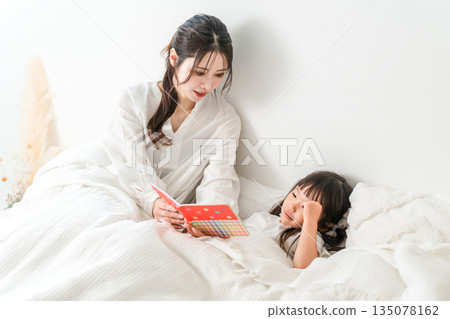Mother reading a picture book to her child in bed (putting to sleep, nap, reading aloud) Mother reading a picture book to her child in bed (putting to sleep, nap, reading aloud) 135078162