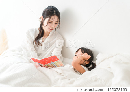 Mother reading a picture book to her child in bed (putting to sleep, nap, reading aloud) 135078163