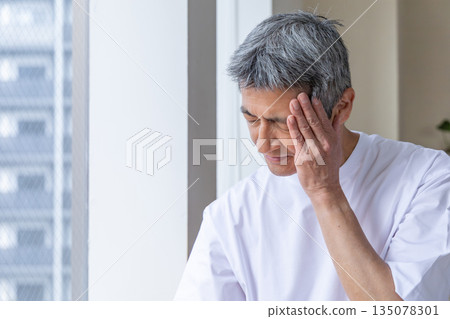 Senior man holding his head by the window 135078301