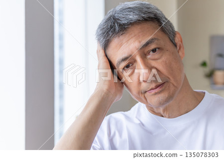 一位老人在窗邊摀著頭。 一位老人在窗邊摀著頭。 135078303