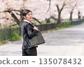 一位身著職業套裝的女商人回頭望去，背景是一排櫻花樹。 135078432