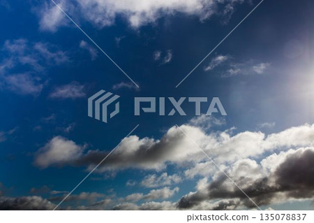 Cloud formations are drifting across deep blue sky in flat design with sunlight glare 135078837