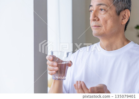 Senior man taking medicine by the window Senior man taking medicine by the window 135079401
