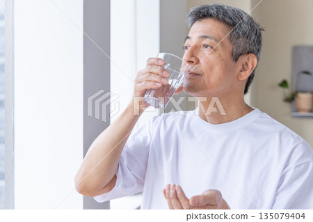 Senior man taking medicine by the window Senior man taking medicine by the window 135079404