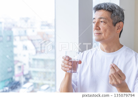 Senior man taking medicine by the window 135079794
