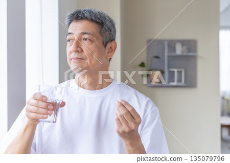 Senior man taking medicine by the window 135079796