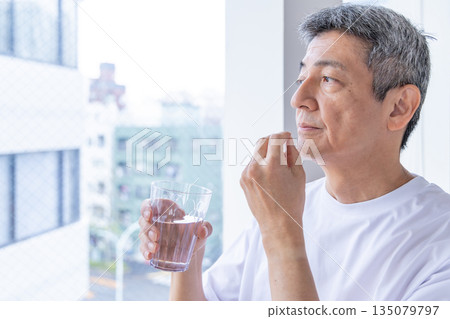 Senior man taking medicine by the window 135079797