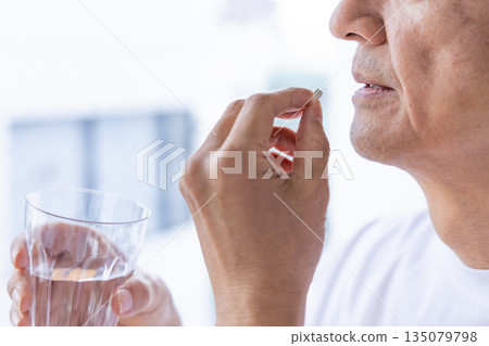 Senior man taking medicine by the window Senior man taking medicine by the window 135079798