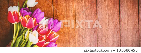 Vibrant tulip bouquet with green stems is resting on rustic wooden plank surface, copy space 135080453