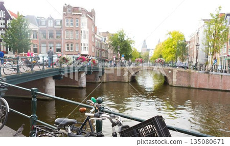 Bicycles are leaning against canal railing under brick arch bridge in flat design with flower boxes Bicycles are leaning against canal railing under brick arch bridge in flat design with flower boxes 135080671
