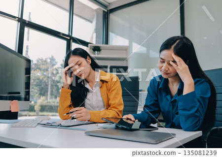 Asian women stressed at work. Teamwork in business with Older Asian women manager. Stressful deadline for young Asian women professional. Asian women stressed at work. Teamwork in business with Older Asian women manager. Stressful deadline for young Asian women professional. 135081239