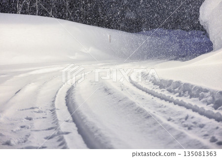 Tire tracks left on snowy roads. Gentle street lights shining on snowy roads late at night. Tire tracks left on snowy roads. Gentle street lights shining on snowy roads late at night. 135081363