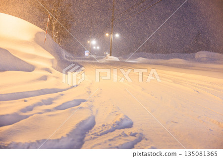 Tire tracks left on snowy roads. Gentle street lights shining on snowy roads late at night. 135081365