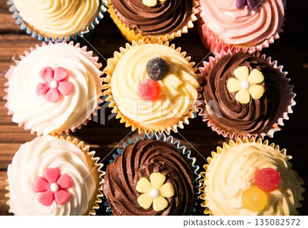 Nine cupcakes are sitting in flat design on wood tabletop with pastel liners and candy decorations Nine cupcakes are sitting in flat design on wood tabletop with pastel liners and candy decorations 135082572