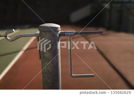 Flat design showing cylindrical net post with horizontal rod and L-shaped crank on clay court 135082629